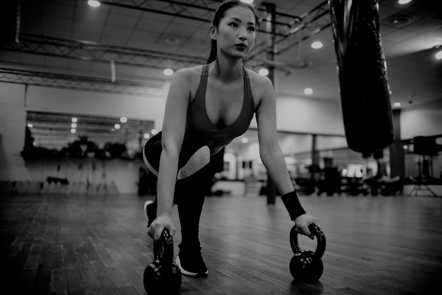 Strong determined ethnic woman stretching body using kettlebells